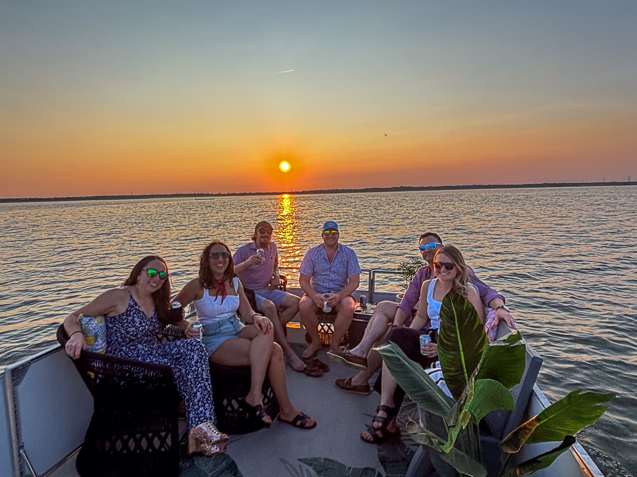 Six guests relaxing with drinks aboard a private Sand Bar Joe's pontoon charter at golden-hour sunset on the Wildwood back bay